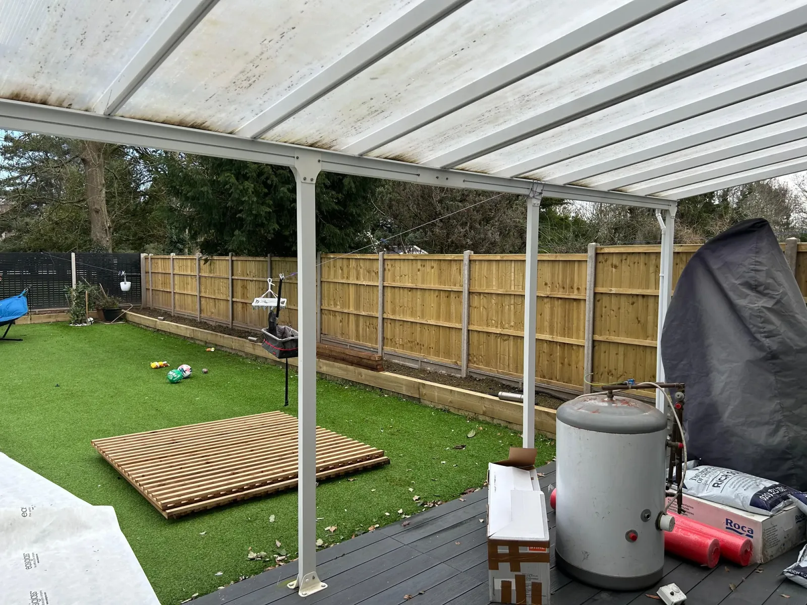 Before: covered patio area with rough grass and existing timber fences in need of refresh